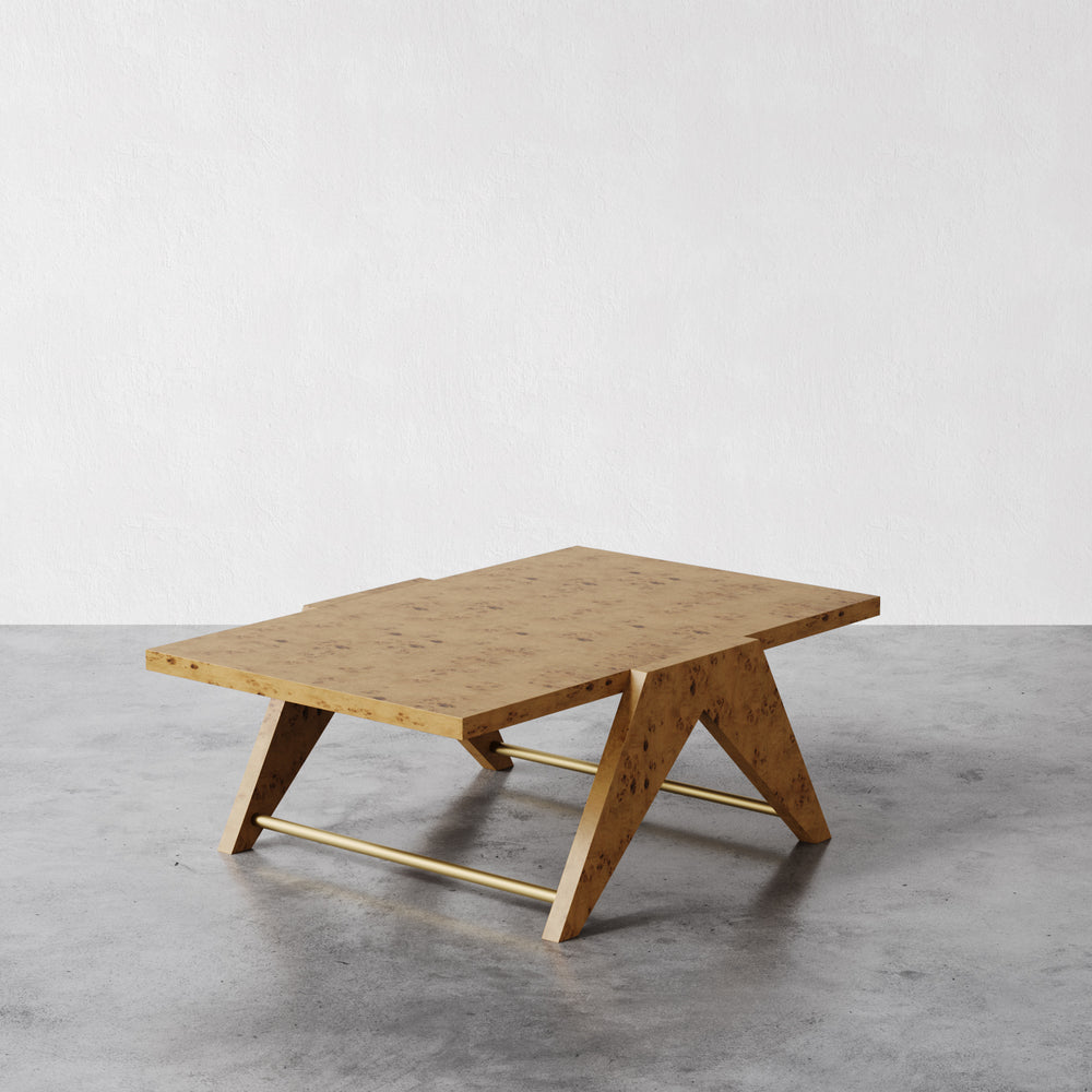Lemieux et Cie Marchand nightstand coffee table with angular legs and brass stretcher, shown on polished concrete floor against white walls.
