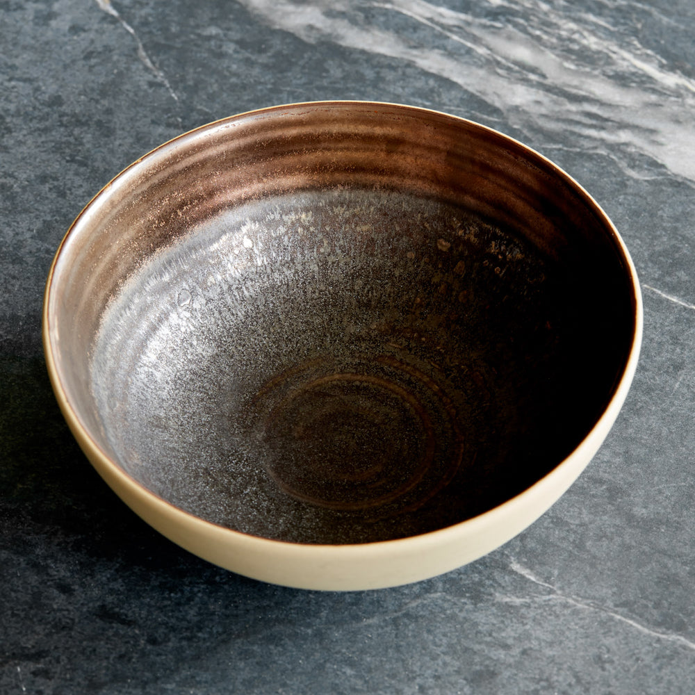 Lemieux et Cie Akita Stoneware Bowl in reactive glaze with copper highlights, ceramic bowl with concentric patterns, shown on dark stone surface.
