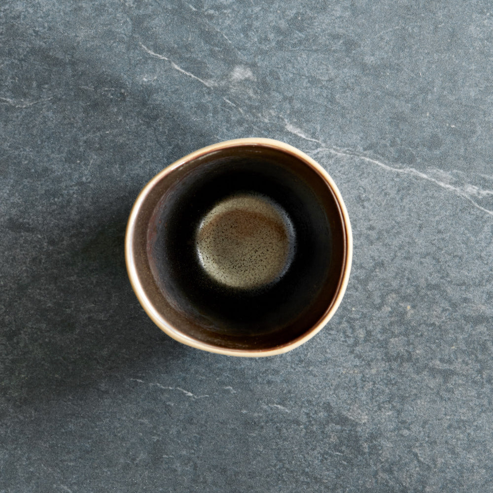 Lemieux et Cie Akita Stoneware Mug in dark glaze with warm rim, ceramic cup shown from above on blue-gray stone surface.