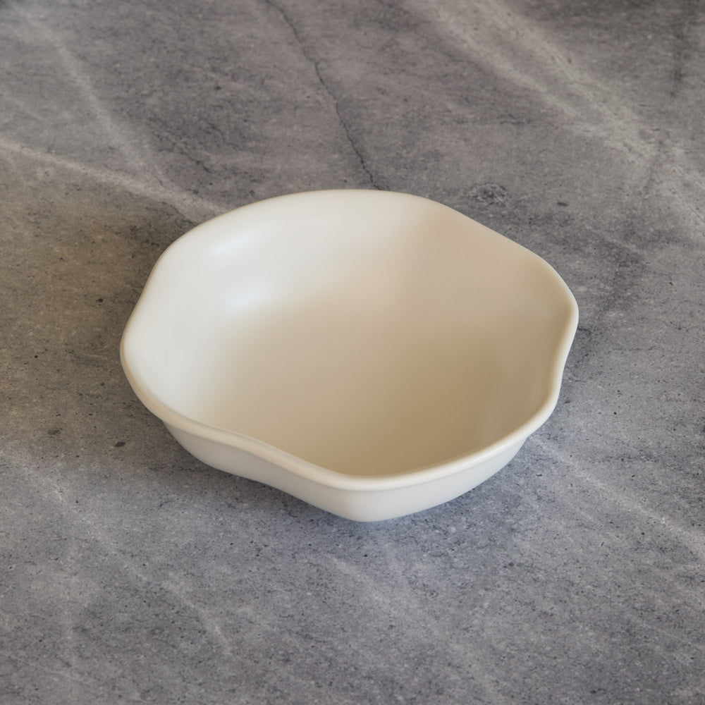 Lemieux et Cie Amorphous Pasta Bowl in warm ivory, organic-shaped ceramic bowl shown on gray concrete surface.
