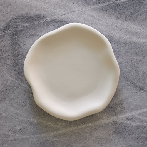 Lemieux et Cie Amorphous Salad Plate in soft white matte glaze, stoneware plate with organic asymmetrical form, shown on concrete surface.