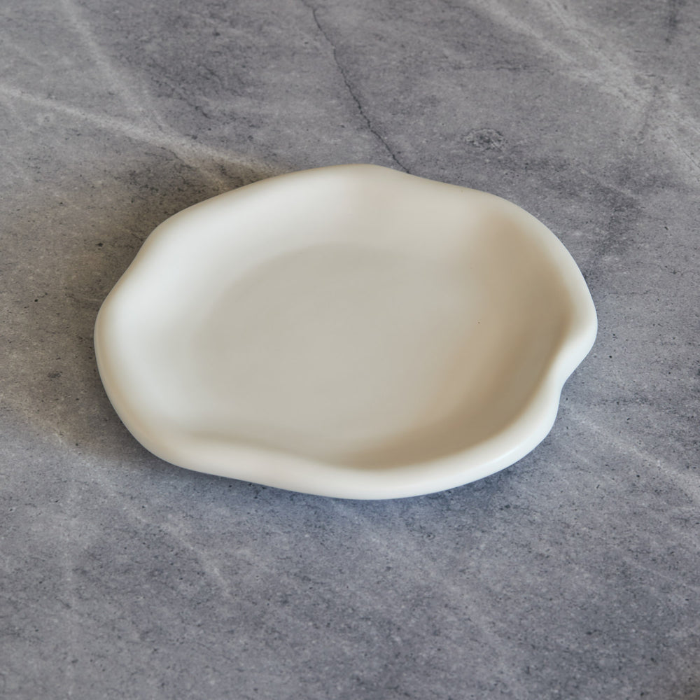 Lemieux et Cie Amorphous Salad Plate in soft white matte glaze, stoneware with organic asymmetrical curves, shown on concrete surface.