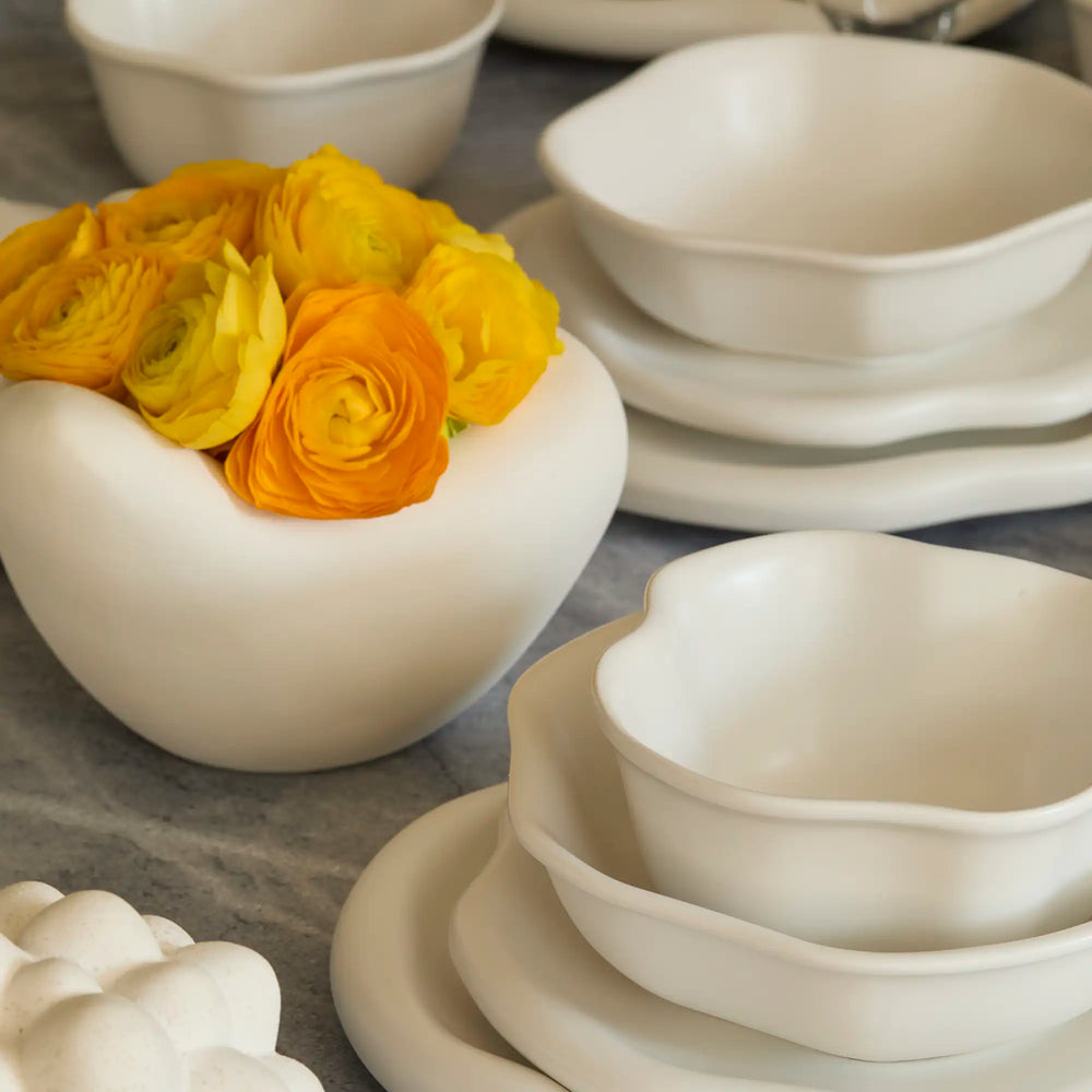 Lemieux et Cie Amorphous Pasta Bowl Set, organic shallow bowls in warm white, displayed on gray stone surface with yellow ranunculus.