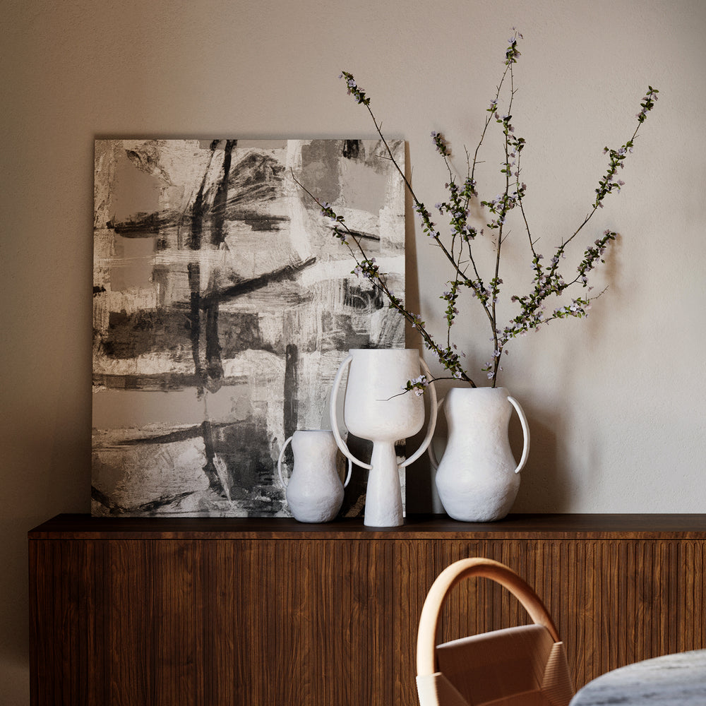 Lemieux et Cie Aquitaine Vase in matte white with ribbon handles, sculptural ceramic vessel styled on wood credenza with abstract art and neutral walls.