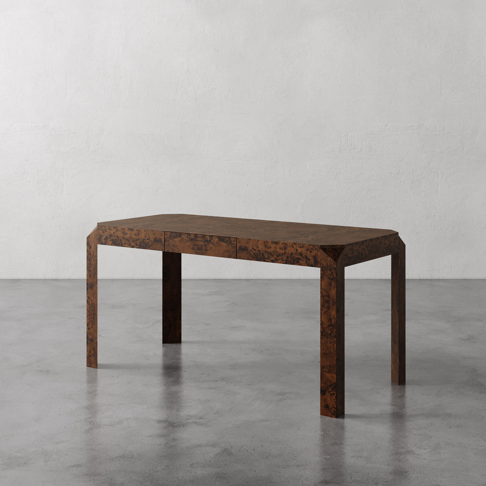 Lemieux et Cie Armand Desk in figured burl veneer with warm brown tones, desk on polished concrete floor against textured white walls.