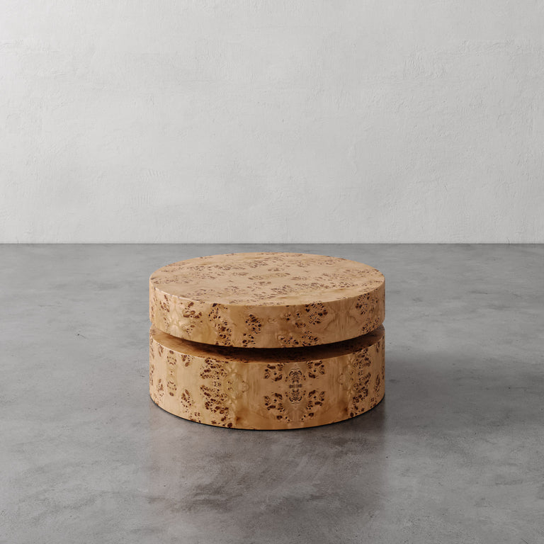 Lemieux et Cie Avenir Coffee Table in warm burl veneer, low round coffee table with tiered form, on grey concrete floor against textured plaster wall.