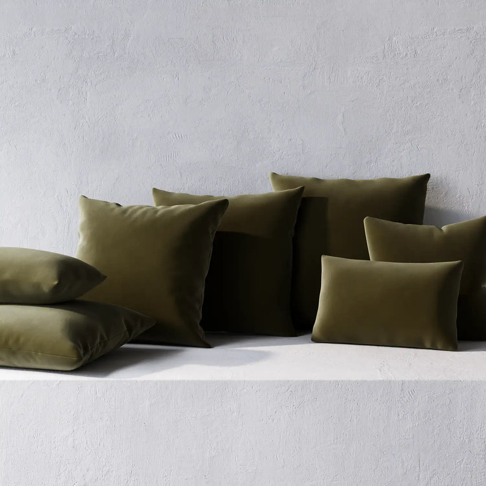 Lemieux et Cie Throw Pillows in olive green, non-welted cushions arranged on white textured plaster ledge against neutral wall