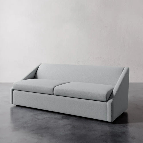 Lemieux et Cie Fontaine Sofa, sculptural architectural silhouette with structured arms and seat cushions, shown on gray concrete floor against textured plaster walls.