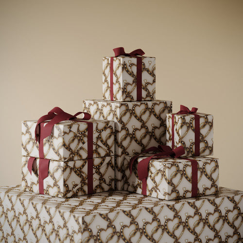Stack of gifts wrapped in Lemieux et Cie Bijou Amour valentine’s day gift wrapping paper depicting jeweled interlocking hearts shaped by the golden age of French haute joaillerie