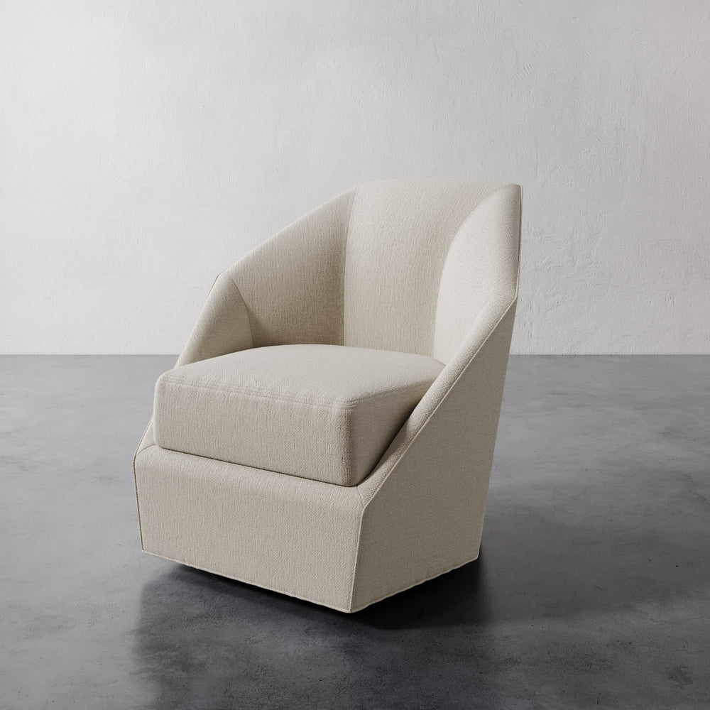 Lemieux et Cie Bijou Swivel Chair in warm ivory, sculptural rounded form with angular wrapped silhouette, on concrete floor against white plaster walls.