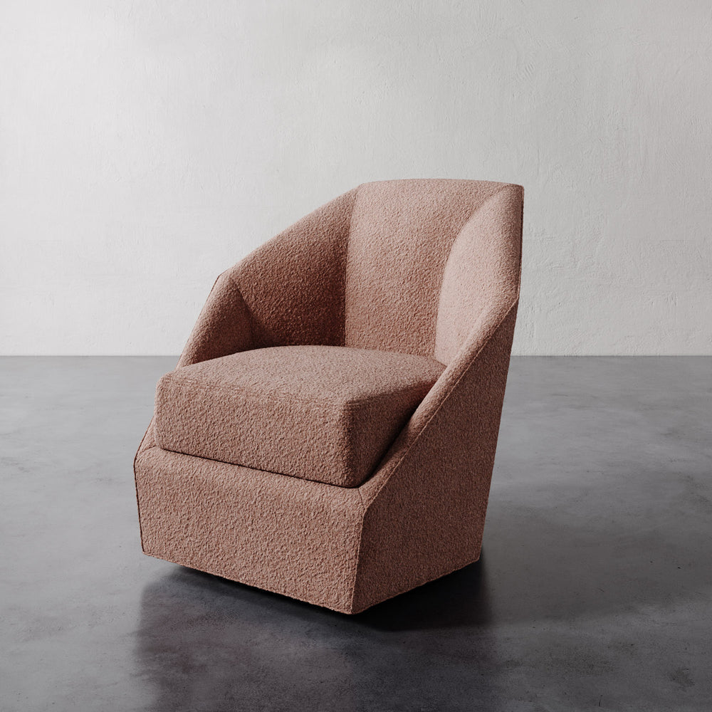 Lemieux et Cie Bijou Swivel Chair in warm blush upholstery, sculptural barrel-back swivel chair with angular geometric form, shown on dark concrete floor against neutral plaster wall.