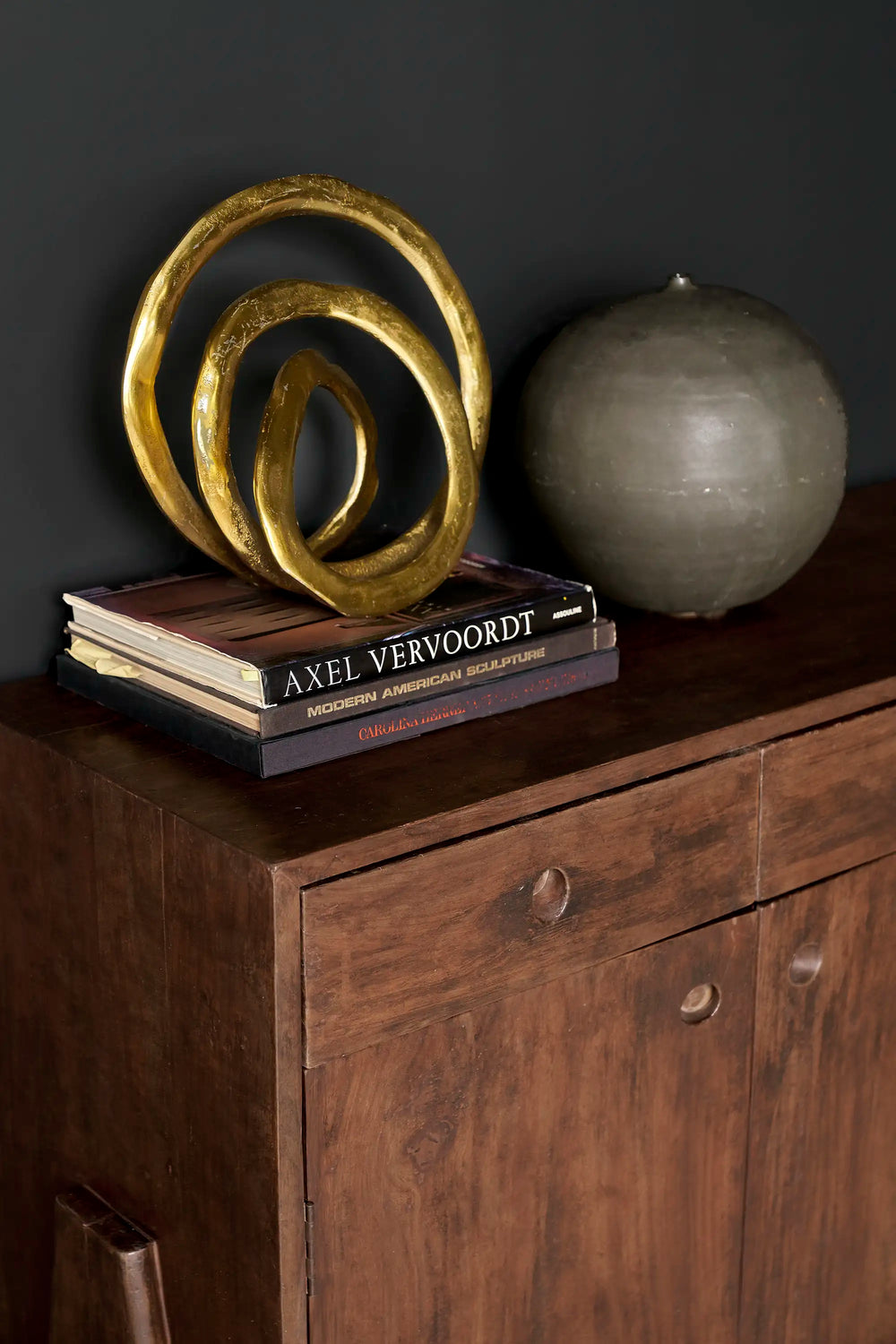 Decorative gold spiral sculpture on books with a black ceramic sphere on a vintage jeanneret cabinet