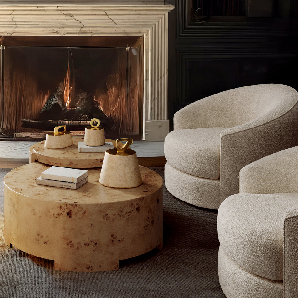 Lemieux et Cie Bocal Lidded Pot in travertine with hand-cast brass handle, sculptural vessel on burled wood coffee tables beside bouclé seating, fireplace surround with warm light.