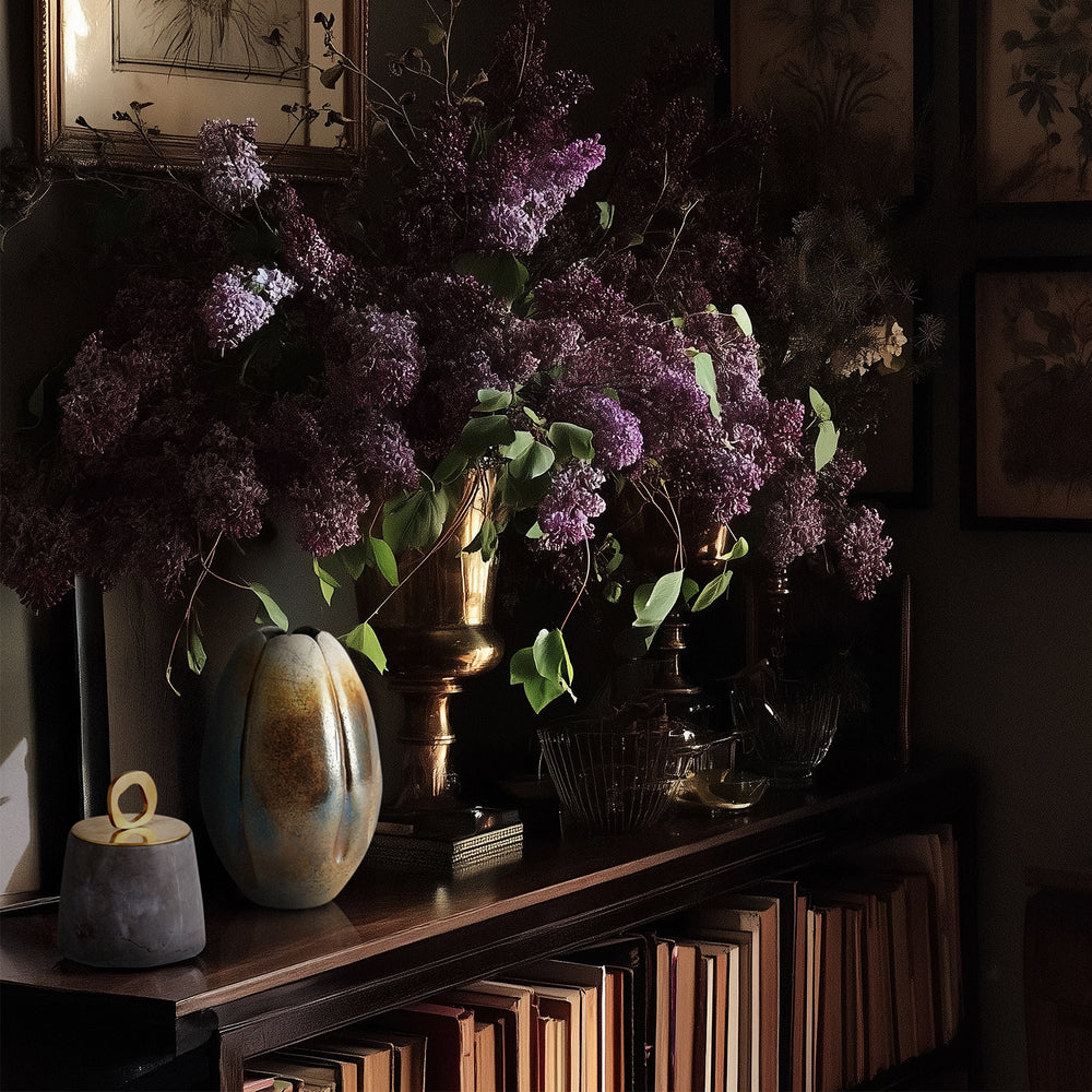 Lemieux et Cie Lafleur Vase, organic rounded ceramic form in warm green glaze, styled on dark wood credenza with purple lilacs and glassware in moody interior.