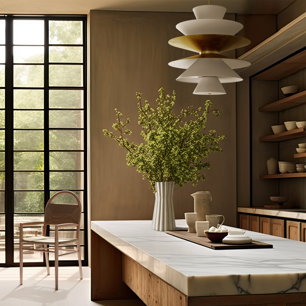 Lemieux et Cie La Brume chandelier with tiered white and brass shades, sculptural pendant hung above marble-topped island in a warm-toned kitchen.
