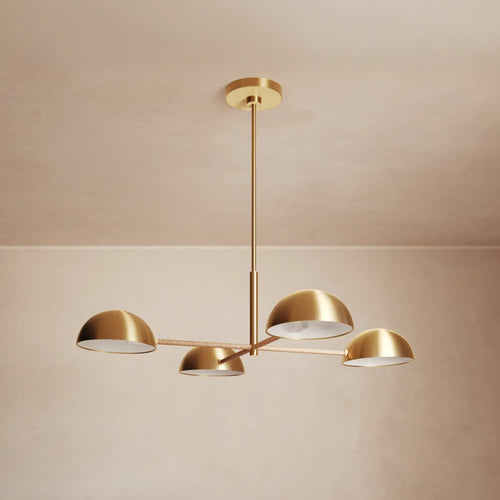 Lemieux et Cie Balleroy chandelier in brass with rattan-wrapped arms, four dome shades suspended on slender stems against neutral plaster walls.