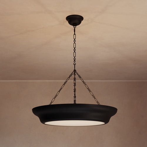 Lemieux et Cie Lenoir Chandelier, sculptural iron bowl form in dark matte finish, suspended by chain from neutral plaster ceiling with warm ambient light.