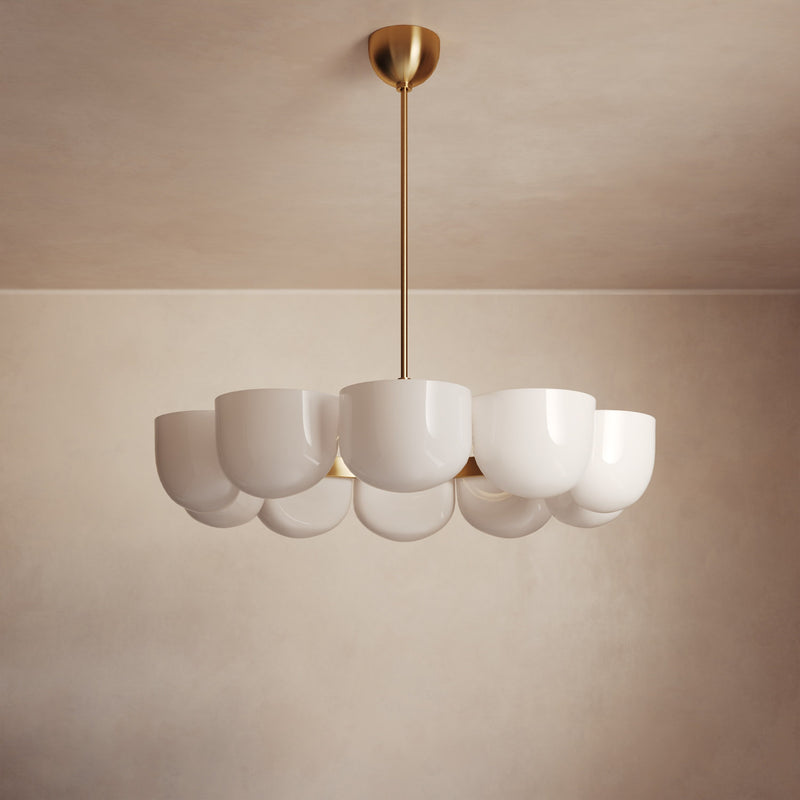 Lemieux et Cie Cheverny Chandelier with white rounded shades and brass stem, suspended against neutral plaster walls and ceiling in soft warm light.