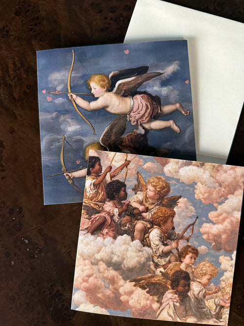 Lemieux et Cie Grecian Cherub Greeting Card Set in classical motif, printed on linen paper, shown on dark burl wood surface beside white envelope.