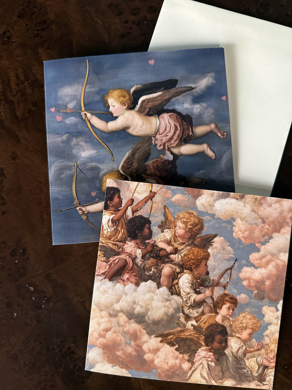 Lemieux et Cie Grecian Cherub Greeting Card Set in classical motif, printed on linen paper, shown on dark burl wood surface beside white envelope.