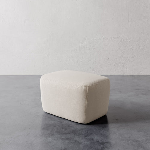 Lemieux et Cie Aurélie Ottoman in ivory, low-profile ottoman with softly rounded rectangular form, shown on polished concrete floor against textured plaster walls.