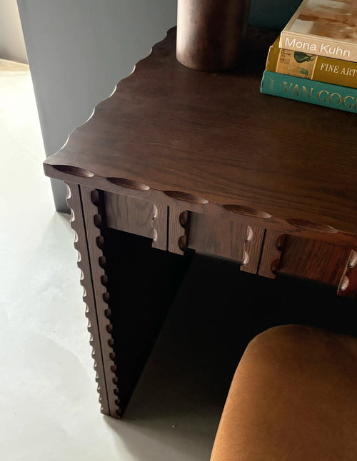 Lemieux et Cie Marchand Desk in walnut oak finish with scalloped edges, open-shelf desk styled with books and vase against white walls.