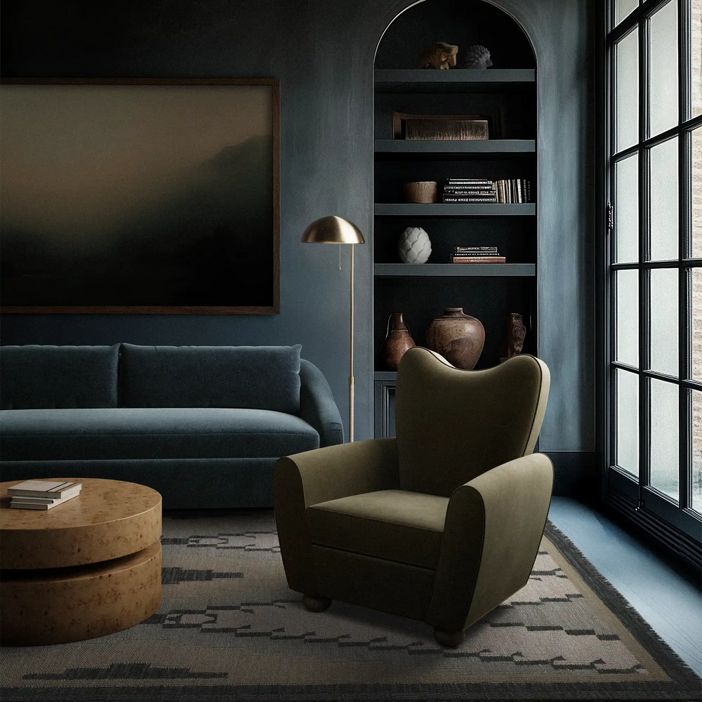 Lemieux et Cie Cornet floor lamp with sculptural dome shade in white cast plaster, standing beside an olive wingback chair in a moody blue sitting room with arched built-in shelving.