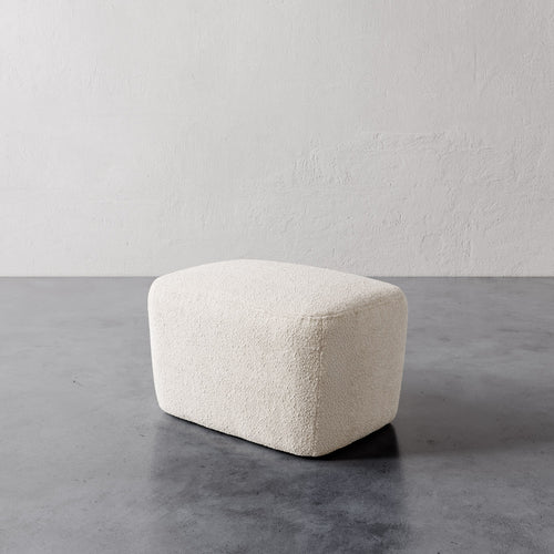 Lemieux et Cie Aurélie Ottoman in ivory, low rounded ottoman with organic sculptural form, shown on polished concrete floor against textured plaster walls.