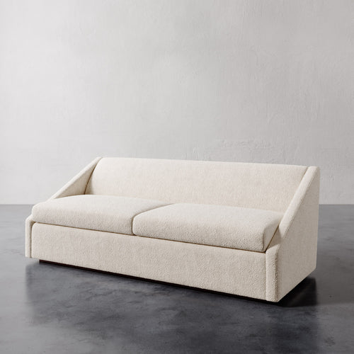 Lemieux et Cie Fontaine Sofa in ivory bouclé upholstery, low-profile sofa with architectural frame, shown on polished concrete floor against textured plaster wall