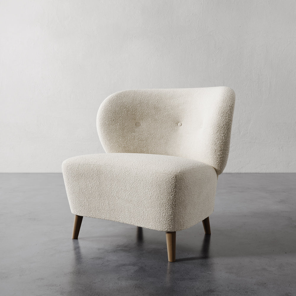 Lemieux et Cie Tourenne Chair with tapered legs in ivory bouclé, organic rounded form with button-tufted back, on concrete floor against neutral wall.