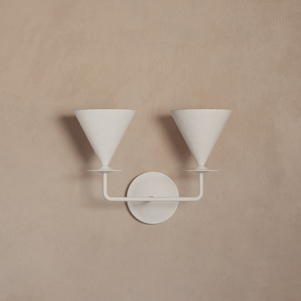 Lemieux et Cie double-arm sconce in white matte finish, wall-mounted light fixture with conical shades, shown on warm neutral plaster wall.