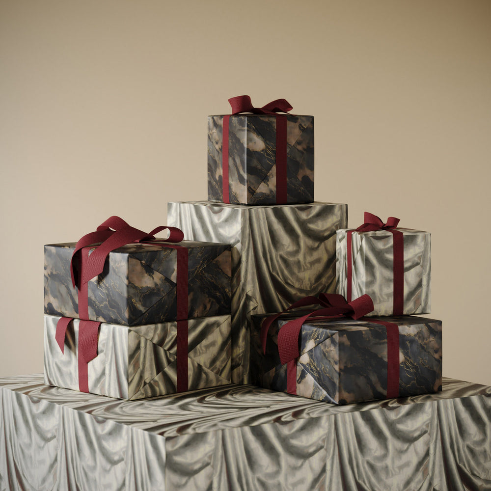 Stack of gifts wrapped in Lemieux et Cie Blue Lapis premium wrapping paper, inspired by deep blue Florentine marble with gold accents, paired with Satin Drape premium gift wrap featuring trompe loeil satin folds in soft neutral tones.