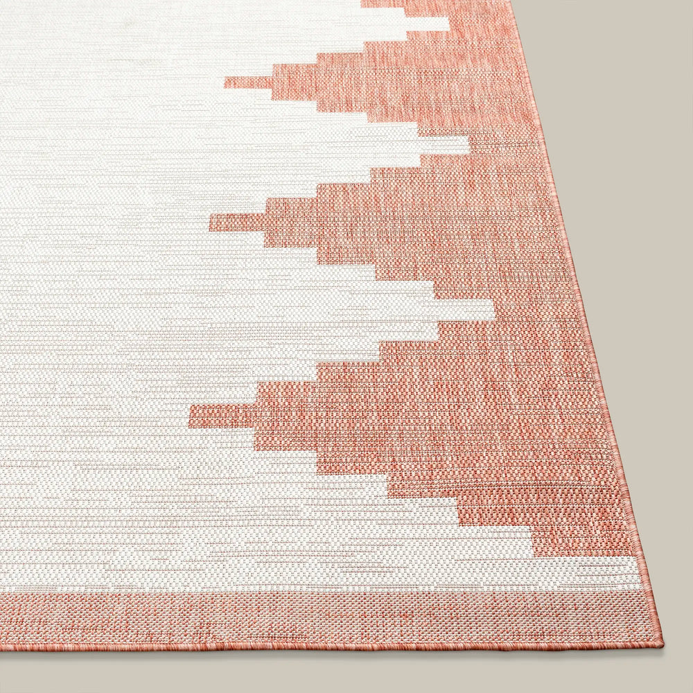 Lemieux et Cie Cottier Outdoor Rug in blush and ivory, woven rug with geometric stepped pattern, shown on neutral floor.