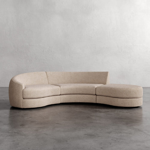 Beige curved sofa on a gray floor with a plain white wall background. Rulmann 3-Piece Left Sectional Eru Boucle