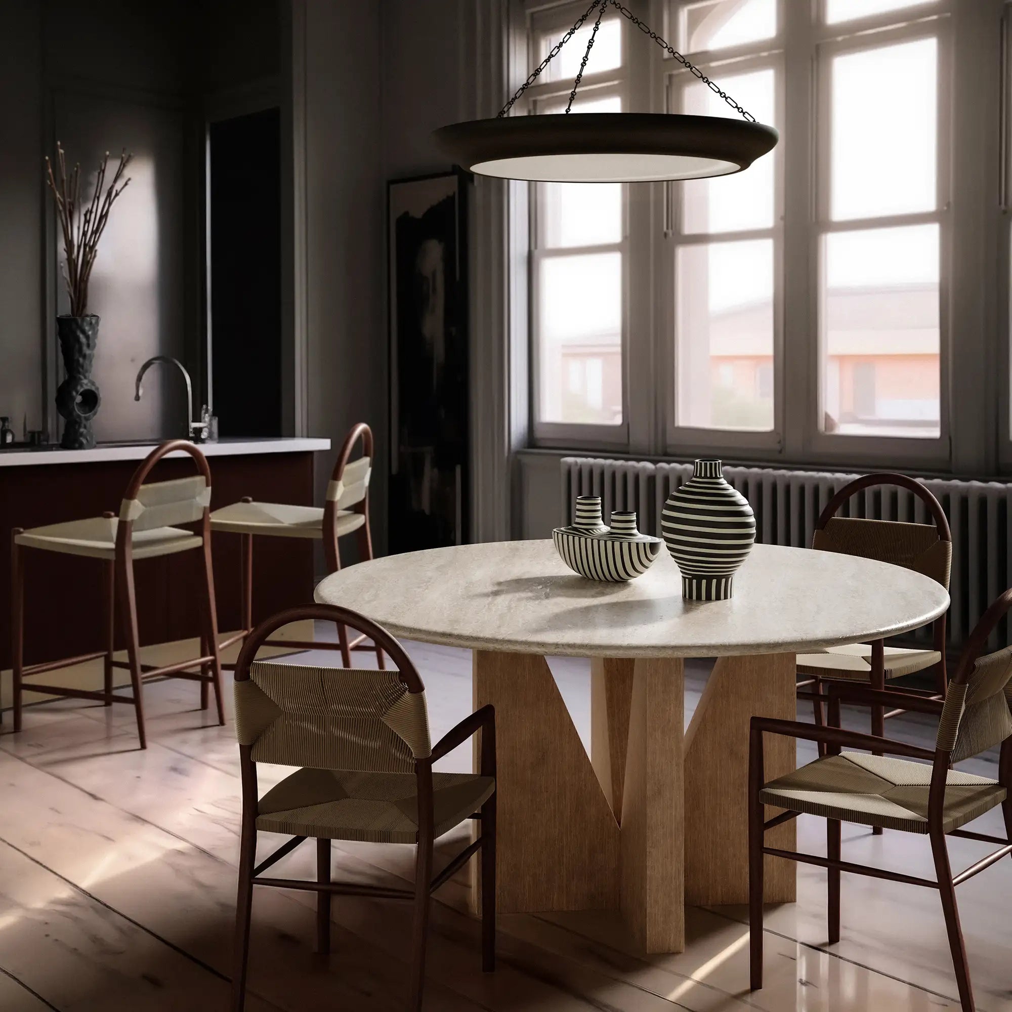 Lemieux et Cie Elysées Dining Table with marble top and geometric base, round dining table surrounded by oak chairs in a light-filled dining room with white walls.