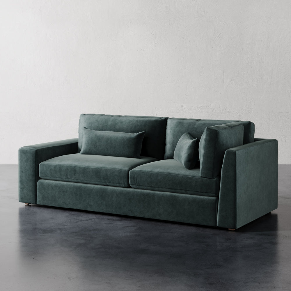 Lemieux et Cie Lacroix Left or Right Return Sofa in deep green velvet, modular sofa with geometric frame, shown on dark concrete floor against white plaster wall.