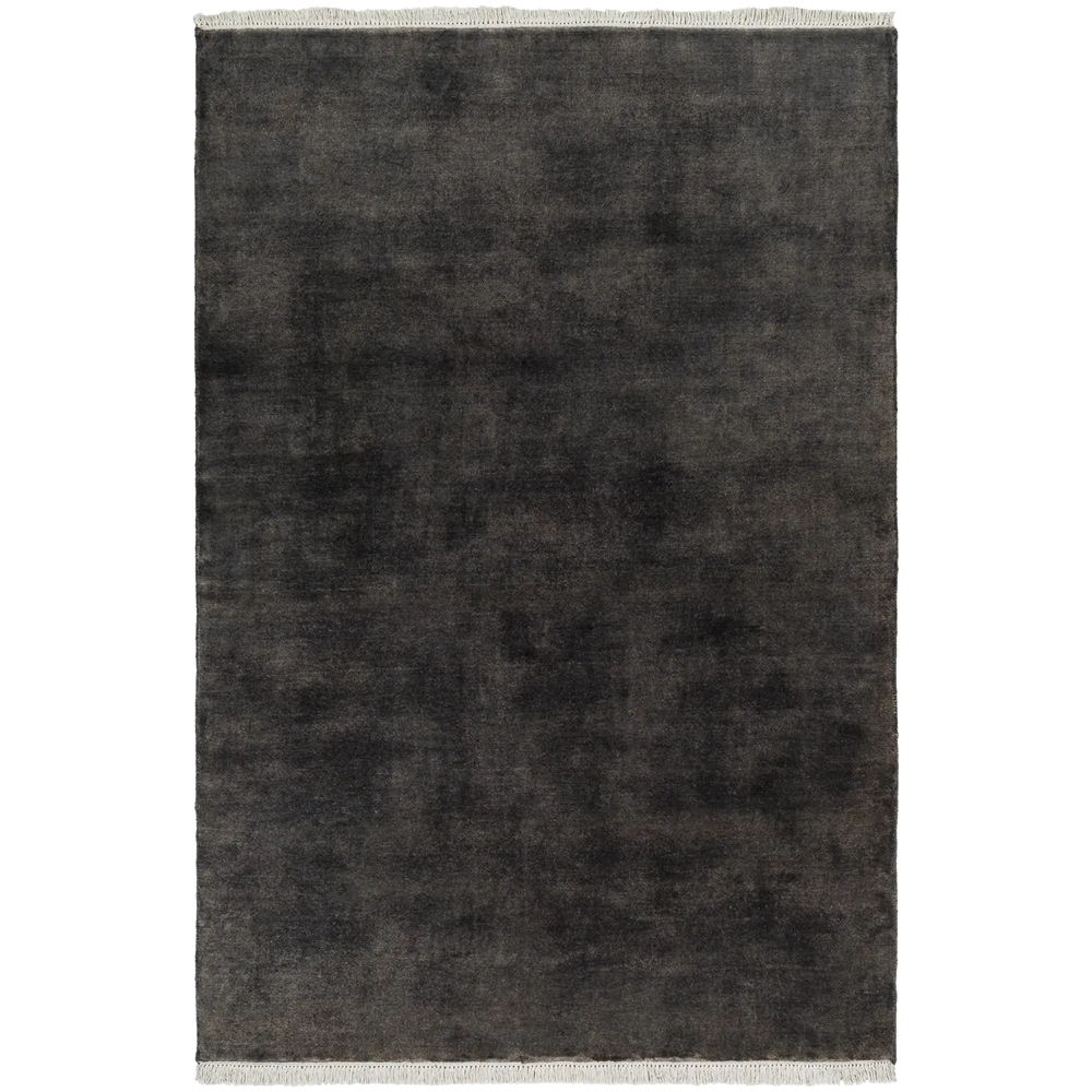 Lemieux et Cie Plume handmade wool rug in charcoal, textured solid with fringe detail, shown on white studio backdrop.