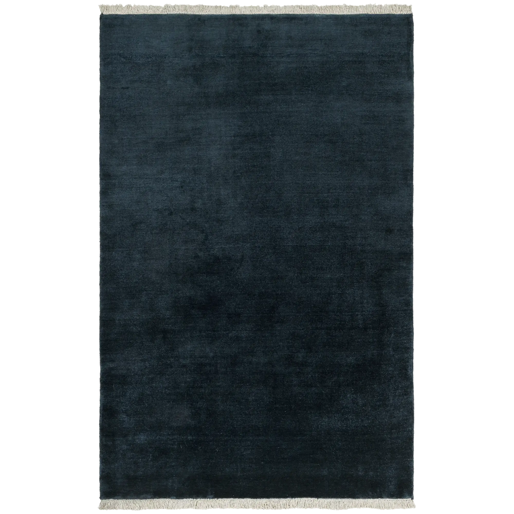 Lemieux et Cie Plume handmade wool rug in dark indigo with fringe detail, shown on white studio backdrop.