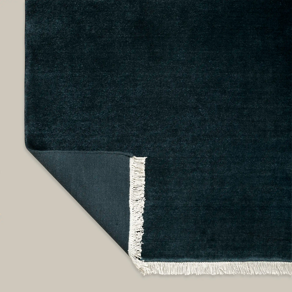 Lemieux et Cie Plume Handmade Wool Rug in Dark Indigo, corner detail showing hand-knotted fringe and woven cotton backing, on neutral backdrop.