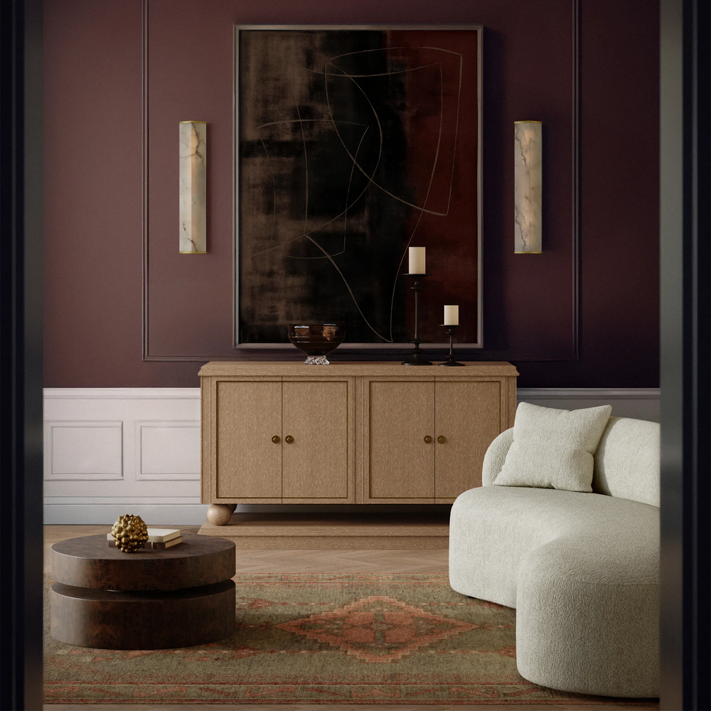 Lemieux et Cie Cleor sconce, a tall rectangular designer lighting fixture with Art Deco influence and mid-century modern sensibility, defined by clean lines and a refined faux alabaster panel, styled in a modern living room with a beige sofa, wooden cabinet, and abstract art on a dark wall.