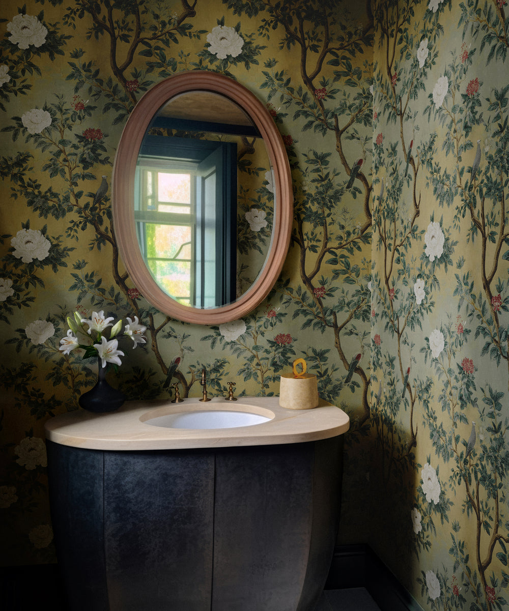 Bathroom styled with Lemieux et Cie Fresco Floral antique chinoiserie wallpaper, featuring a weathered finish and birds in a vintage chinoiserie mural design, paired with an oval mirror and sink.