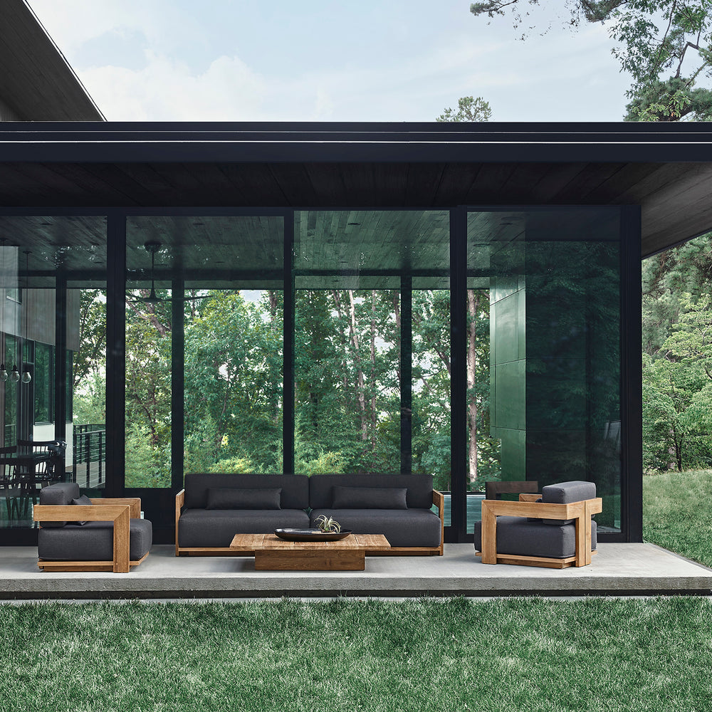 Lemieux et Cie S2 Teak 62" Sofa in dark upholstery with teak frame, outdoor sofa styled on covered patio with glass walls and lawn.