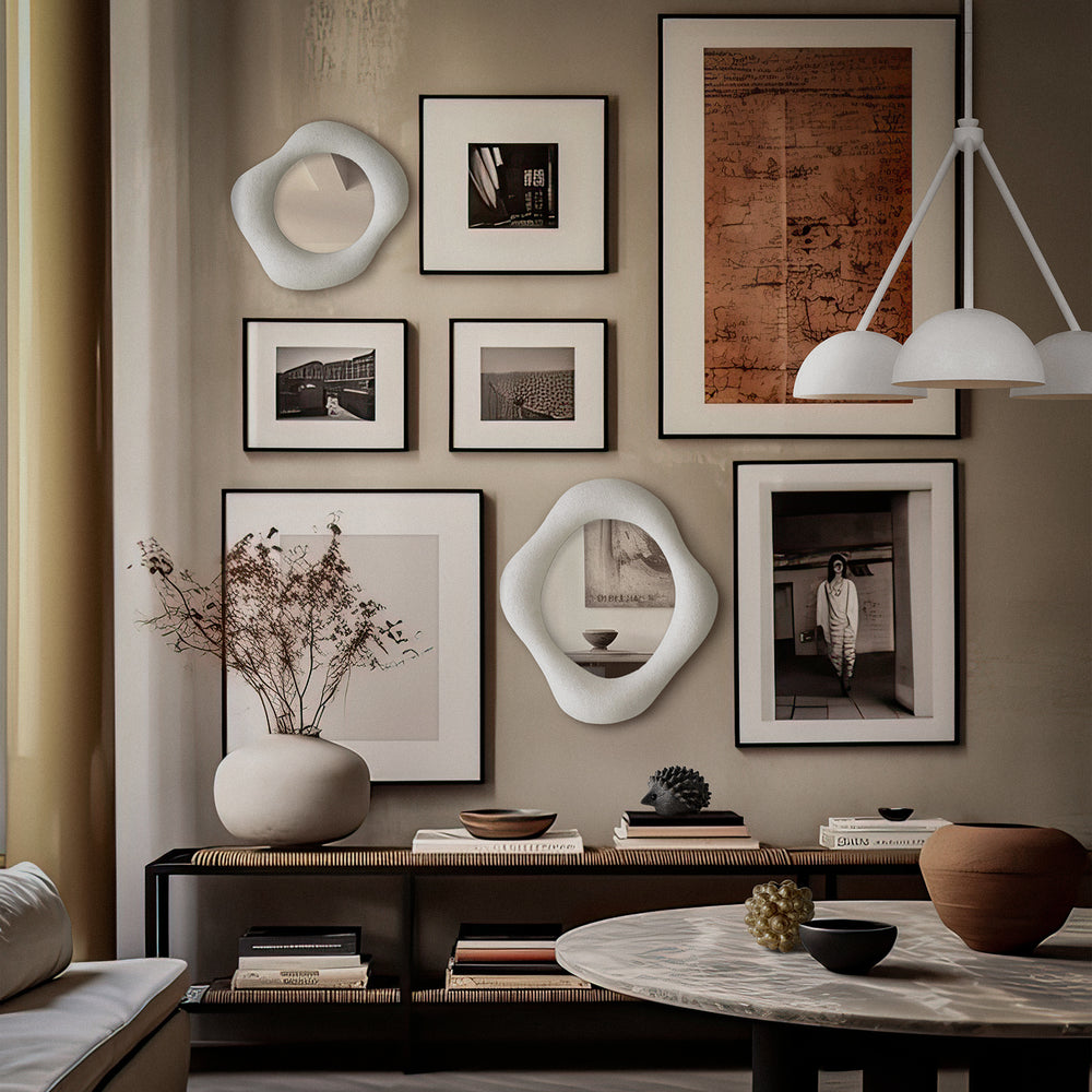 Lemieux et Cie hand-sculpted mirror with asymmetrical organic frame, displayed on neutral plaster wall among black-framed photography and warm wood console in sitting room.