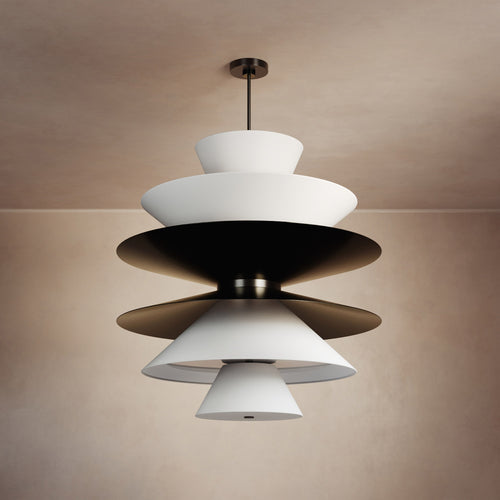 Lemieux et Cie sculptural chandelier with tiered shades in white and dark tones, suspended against warm neutral plaster walls in soft ambient light.