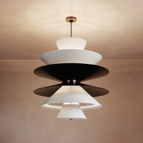 Lemieux et Cie sculptural chandelier with tiered white and dark shades, suspended from ceiling in warm interior light.