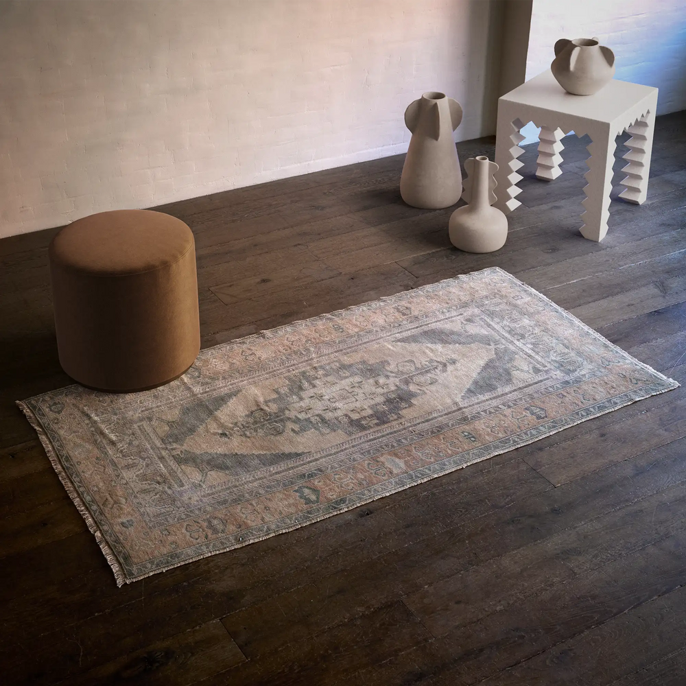 Lemieux et Cie Vintage 1960's Anatolian rug in faded tan and blue, handwoven vintage rug on dark wood floors beside ceramic vases and ottoman.