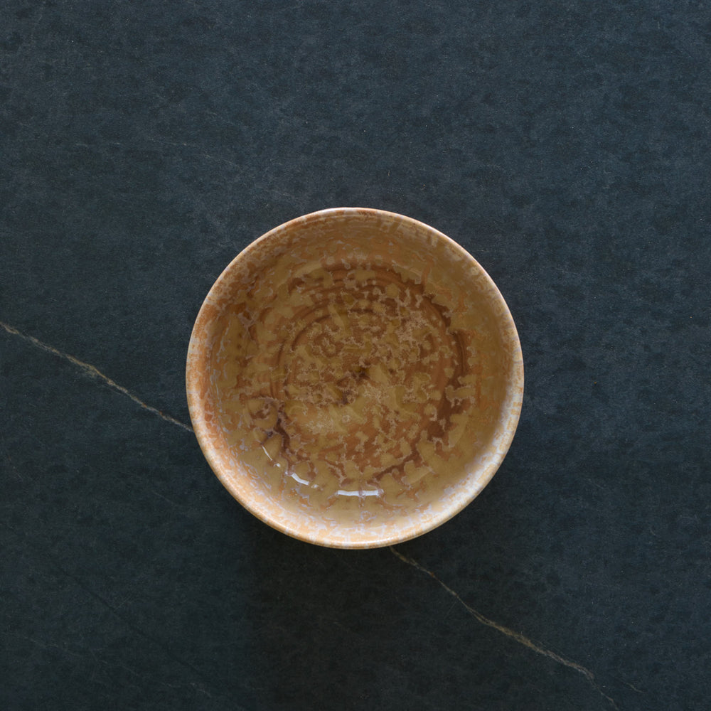 Lemieux et Cie Hanami Stoneware Bowl in Sand, reactive glaze with tonal shifts and crackling, shown overhead on dark stone flooring.