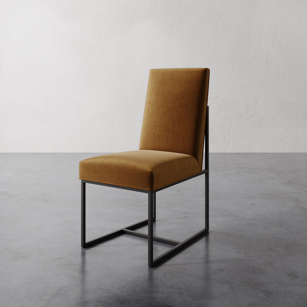 Lemieux et Cie Dupont Dining Side Chair in warm ochre upholstery with slender black frame, shown on concrete flooring against textured plaster walls.
