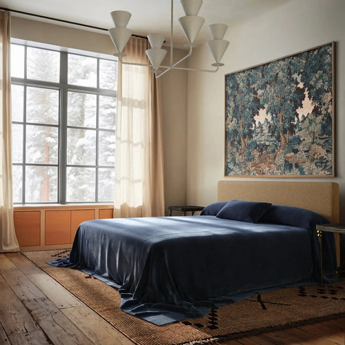 Lemieux et Cie Heavy Linen Coverlet in Indigo, draping a bed in a bedroom with wood floors, neutral walls, and soft daylight from gridded windows.