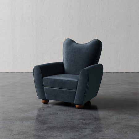 Lemieux et Cie Danielle Chair in deep charcoal upholstery, sculptural wingback armchair with rounded arms and turned feet, on polished concrete floor against textured plaster walls.